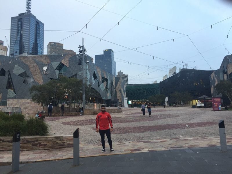 Dani en Melbourne chico joven en una calle de Melbourne con cielo cubierto y los edificios a la izquierda.